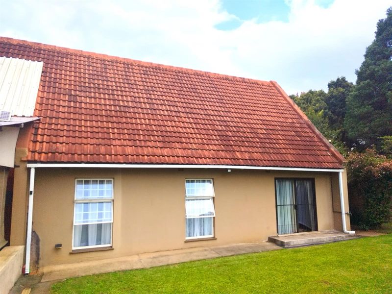 Rear view of the property featuring a pitched tiled roof, sliding glass door access, and a paved walkway leading to the garden.