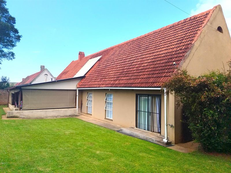 Rear view of the house featuring a pitched tiled roof, a covered patio area, and a well-maintained lawn.