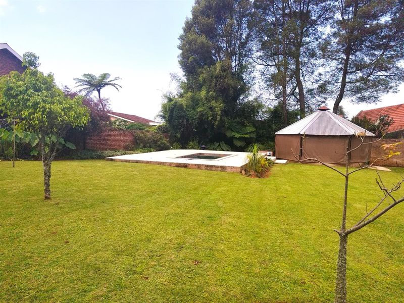 Spacious garden area featuring a paved pool surround and a detached gazebo structure set within a mature, landscaped backyard.