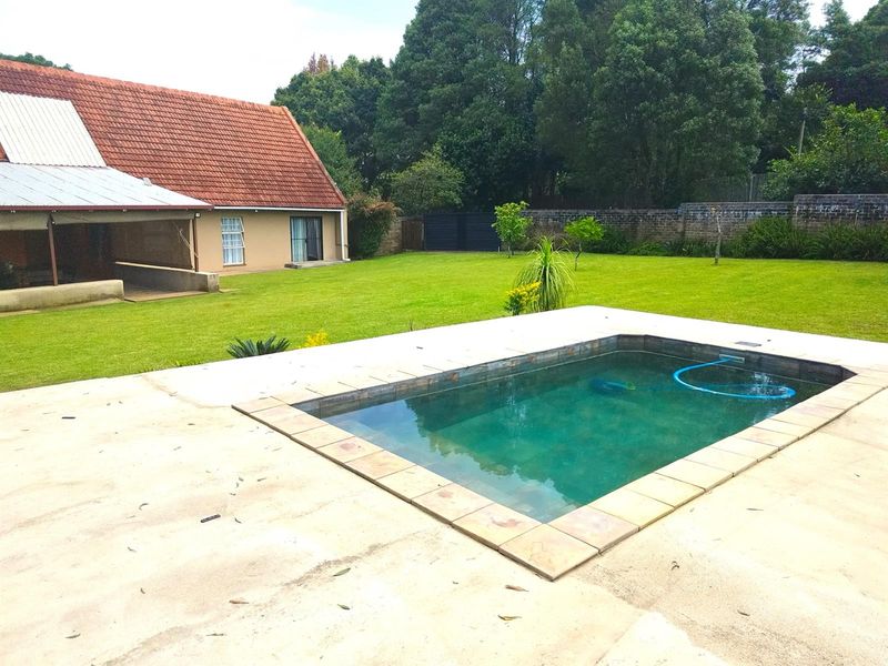 A spacious rear garden featuring a swimming pool with a concrete deck, set against the backdrop of the house and mature trees.