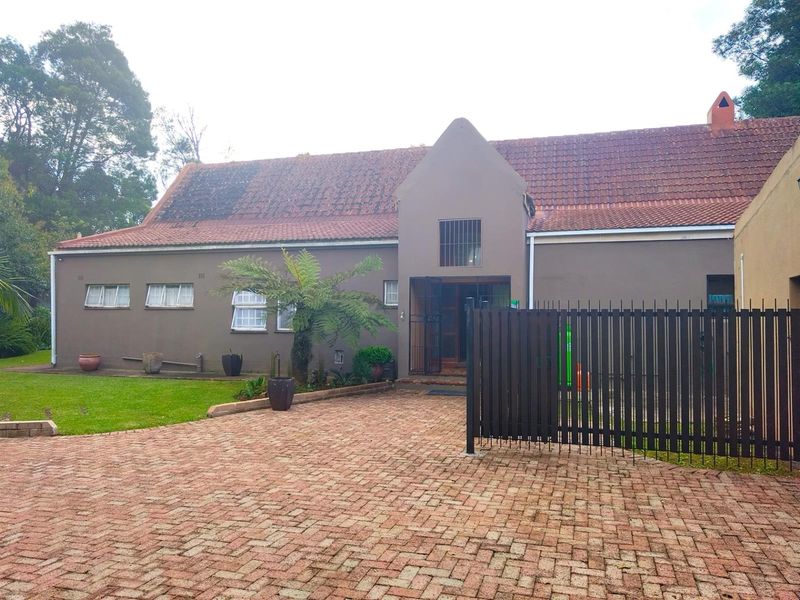 Front elevation of a house featuring a paved driveway, metal security gate, and a tiled roof.