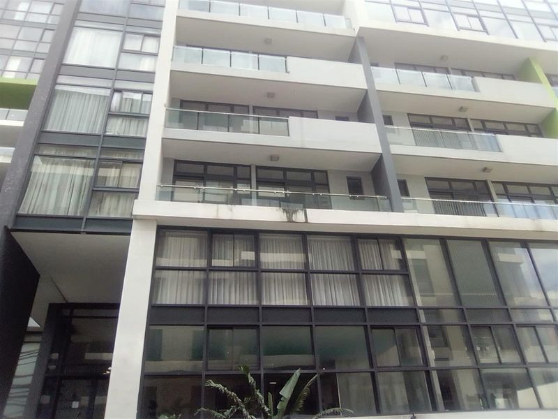 Exterior view of a modern multi-story apartment building featuring glass balcony railings and large aluminium-framed windows.