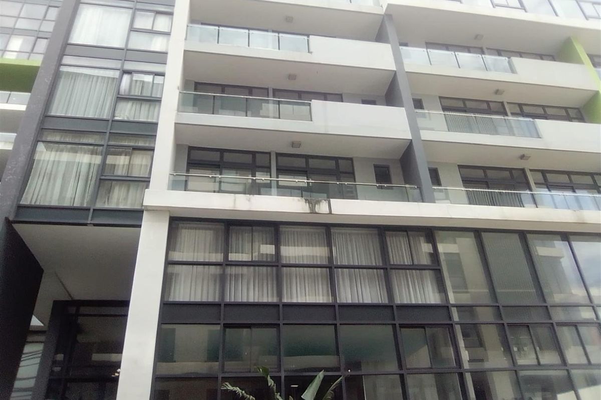 Exterior view of a modern multi-story apartment building featuring glass balcony railings and large aluminium-framed windows.