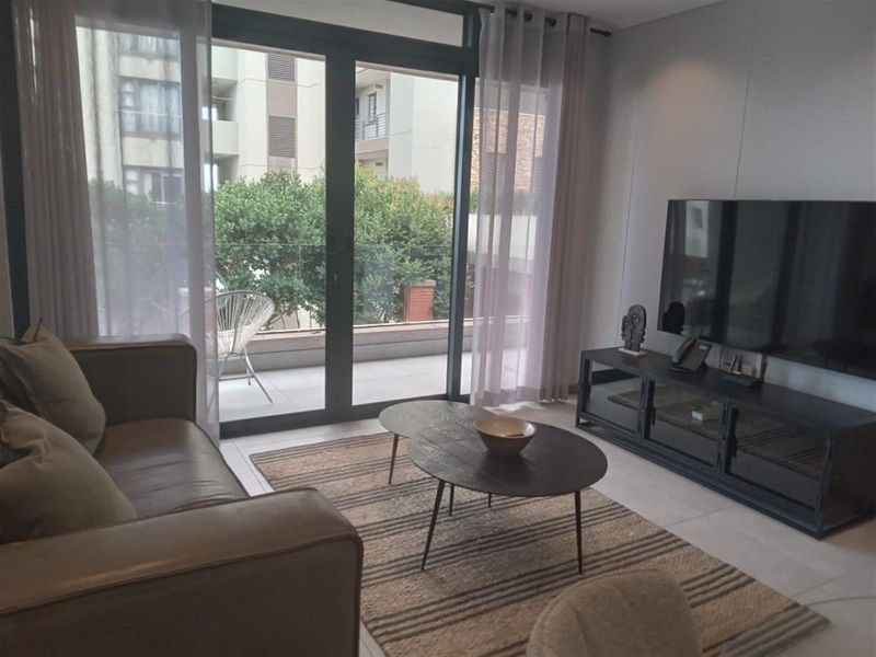 A modern living room featuring large sliding glass doors that open onto a private balcony with a glass balustrade.