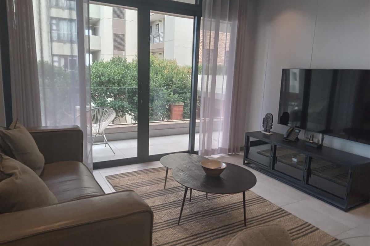A modern living room featuring large sliding glass doors that open onto a private balcony with a glass balustrade.