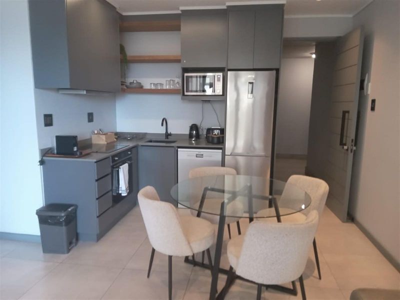 Modern open-plan kitchen featuring sleek grey cabinetry, integrated appliances, and tiled flooring, seamlessly flowing into the dining area.