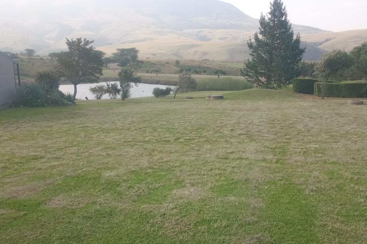 A spacious rear garden featuring a well-maintained lawn, mature trees, and scenic views of the surrounding landscape and nearby pond.
