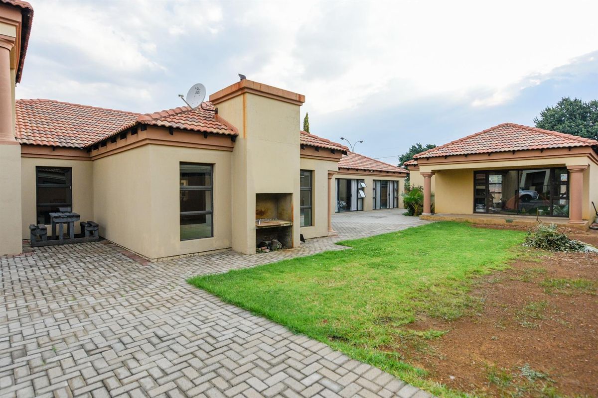 Rear view of the property featuring a paved patio area, built-in braai, and a garden space with tiled roof architecture.