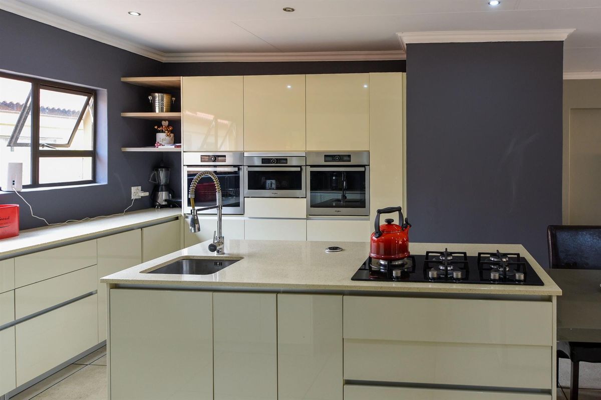 Modern kitchen featuring high-gloss cabinetry, stone countertops, a central island with a gas hob, and integrated built-in appliances.