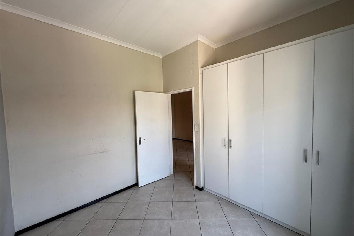A vacant bedroom featuring neutral tiled flooring, built-in white cupboards, and coved ceilings, offering a clean canvas for personalization.