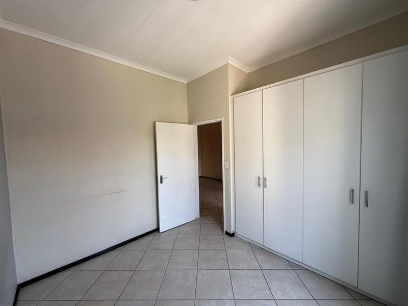 A vacant bedroom featuring neutral tiled flooring, built-in white cupboards, and coved ceilings, offering a clean canvas for personalization.