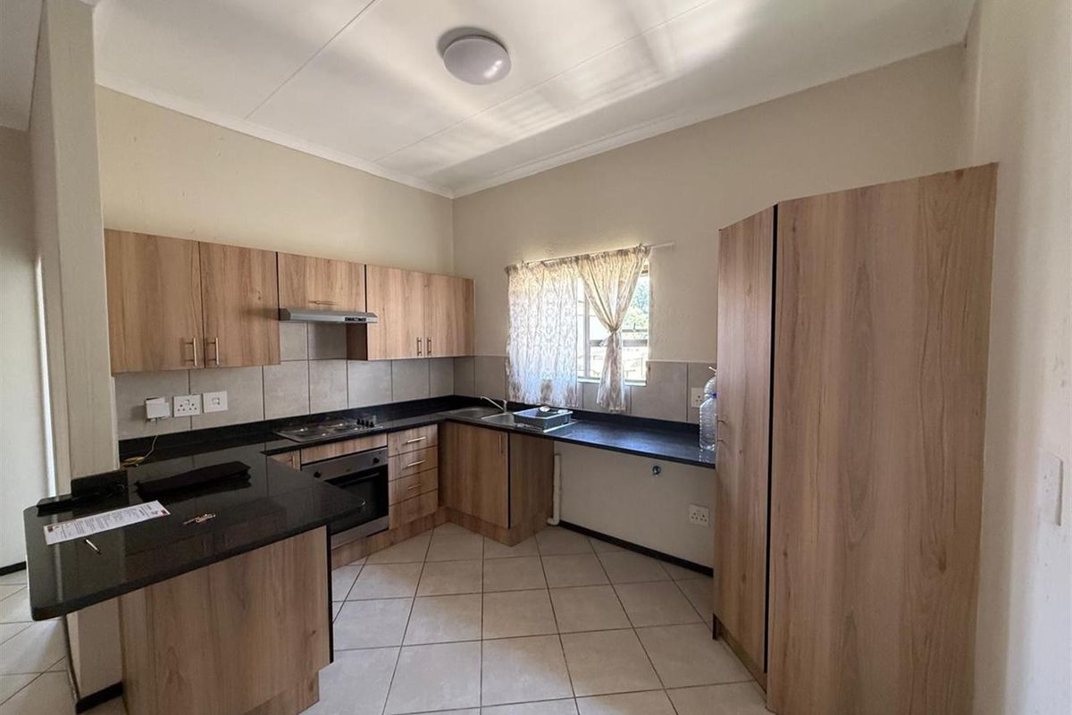 A functional kitchen featuring light wood-finish cabinetry, dark countertops, built-in oven and hob, and tiled flooring.