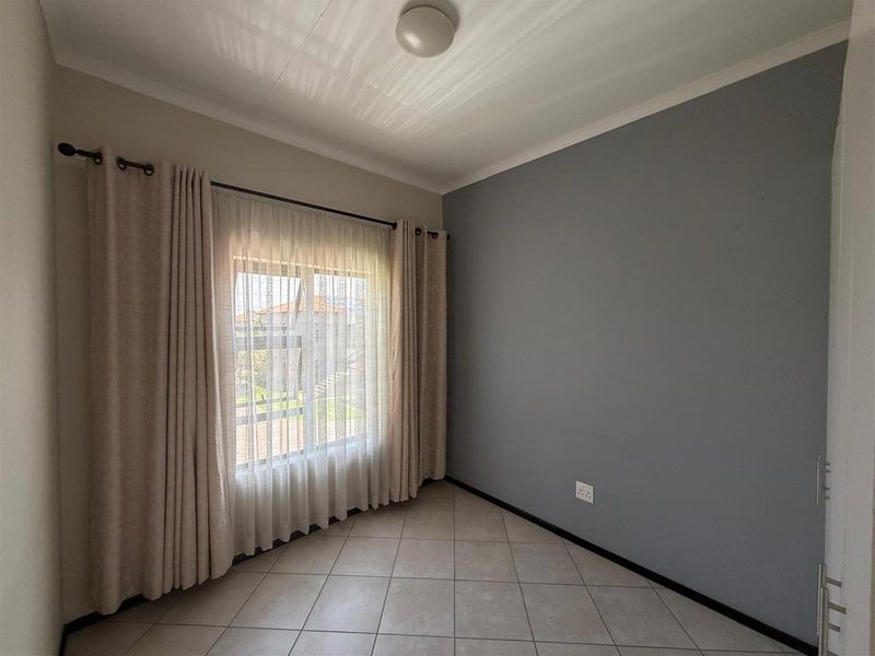 A bright, empty bedroom featuring neutral tiled flooring, a grey accent wall, and a window dressed with curtains.