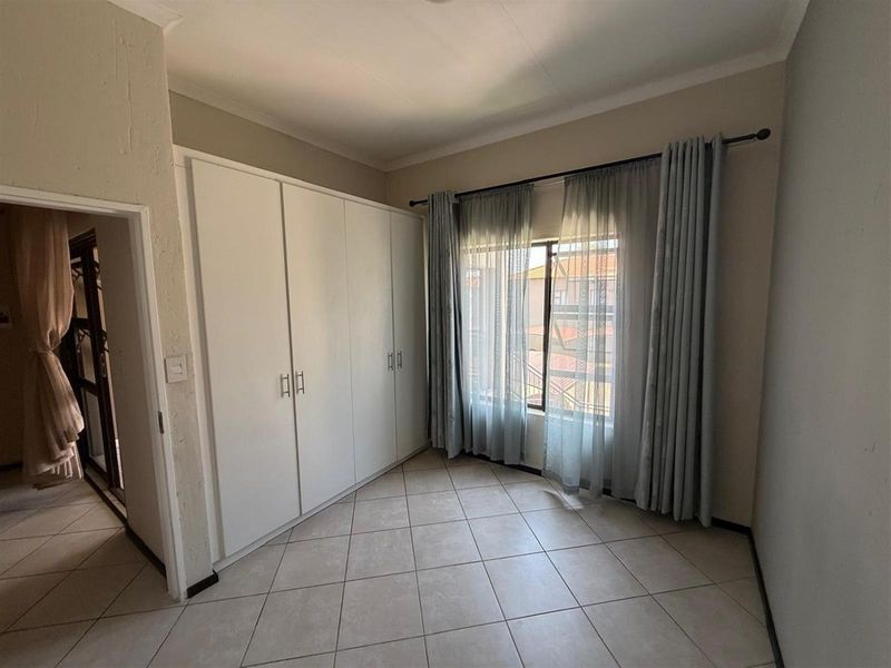 A bright, empty bedroom featuring neutral tiled flooring and ample built-in cupboard storage space.