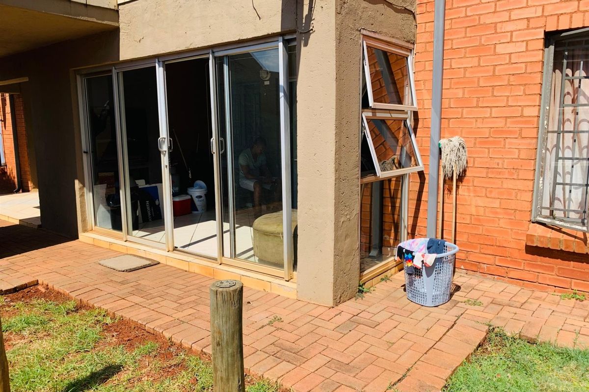 Exterior view of an apartment featuring sliding glass doors, aluminium window frames, and a paved patio area adjacent to a brick facade.
