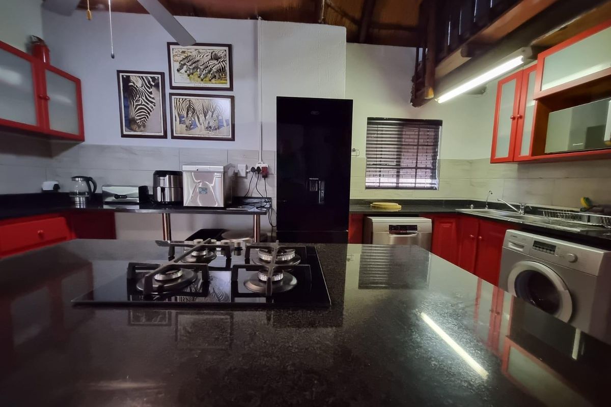 A functional kitchen featuring a central island with a gas hob, granite countertops, and ample built-in cabinetry with a vibrant red finish.