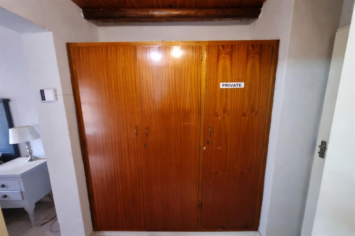 A bedroom featuring a large built-in wooden wardrobe with an exposed timber ceiling beam above.