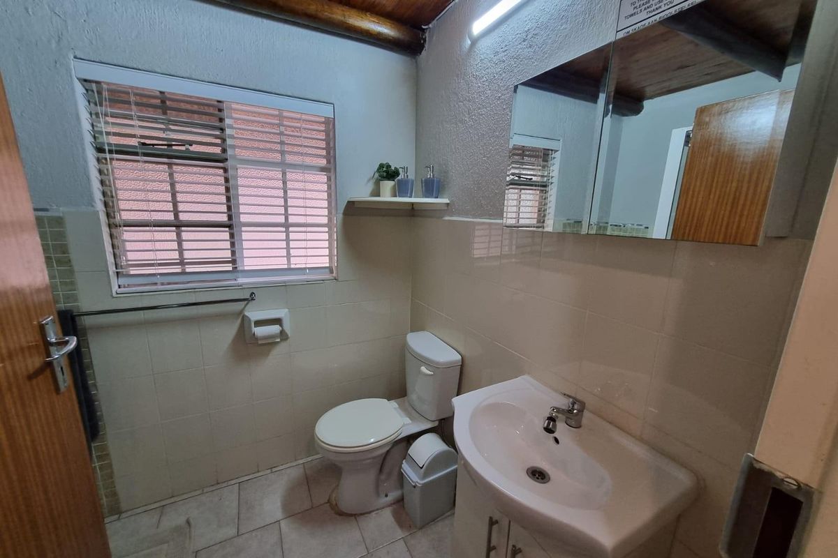A functional bathroom featuring a vanity basin, ceramic toilet, tiled finishes, and timber ceiling beams, providing a practical and well-lit space.