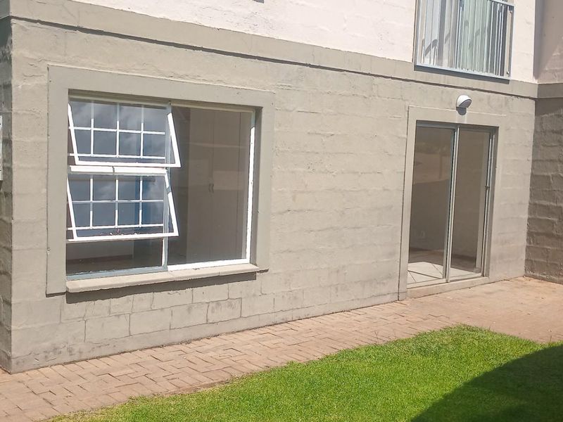 Rear exterior view of the apartment building featuring a paved patio area, sliding glass doors, and casement windows with a small lawn.