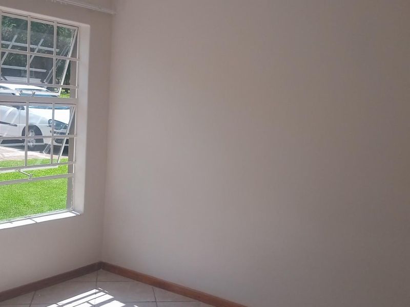 An empty bedroom featuring tiled flooring, neutral walls, and a large window fitted with security bars overlooking the exterior grounds.
