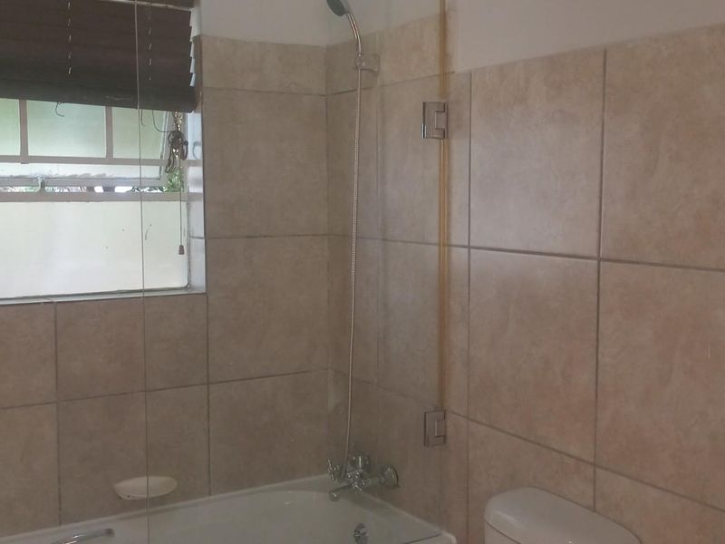 A functional bathroom featuring a bathtub with a shower mixer, glass screen, and neutral wall tiling.