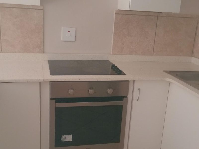 A clean, functional kitchen featuring built-in oven, electric hob, stone countertops, and a double basin sink with tiled backsplash.