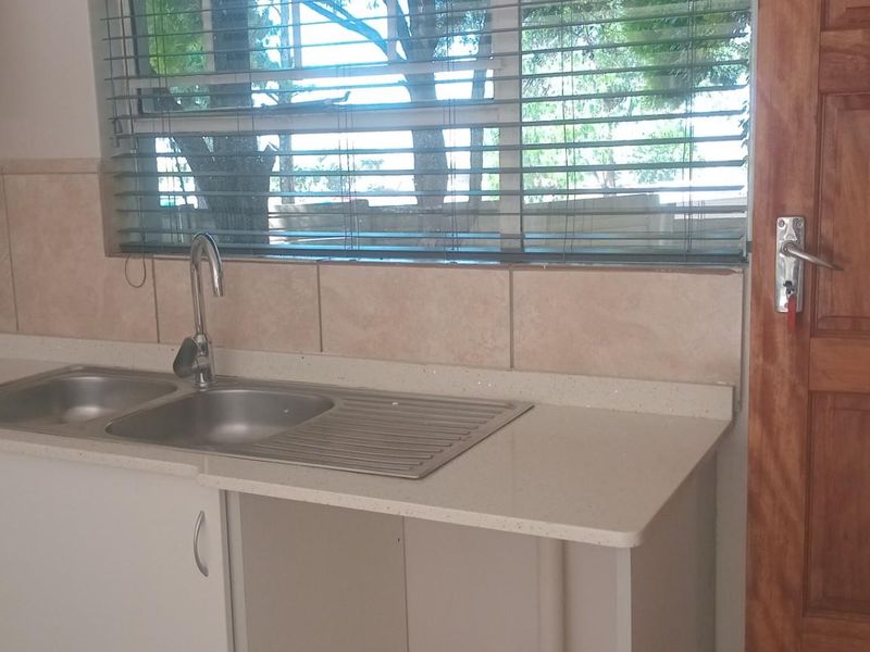 A functional kitchen area featuring a stainless steel double sink, stone countertops, tiled backsplash, and neutral cabinetry, offering a clean and practical workspace.