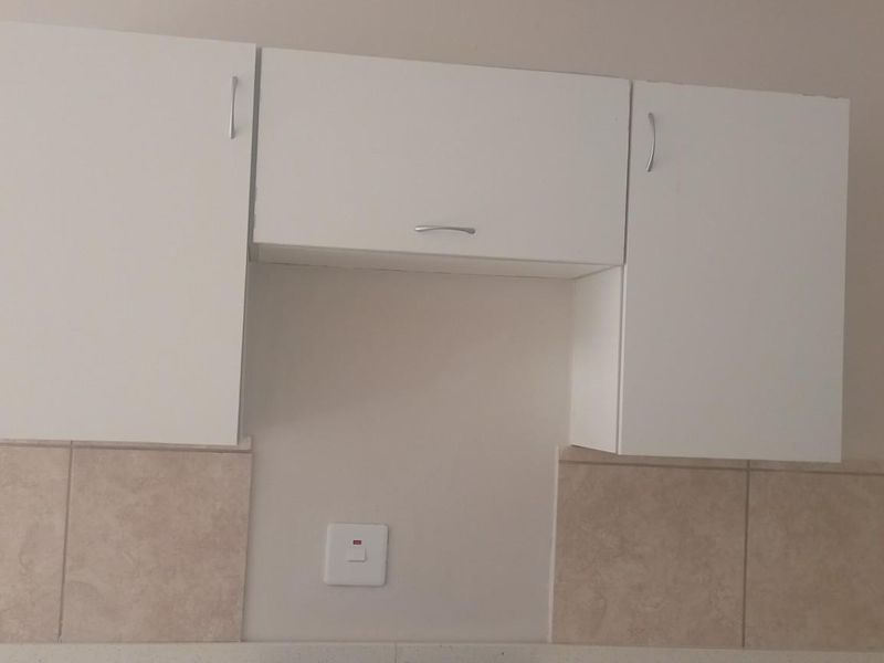 A clean kitchen wall section featuring white overhead cabinetry, neutral tiled splashbacks, and integrated electrical points.