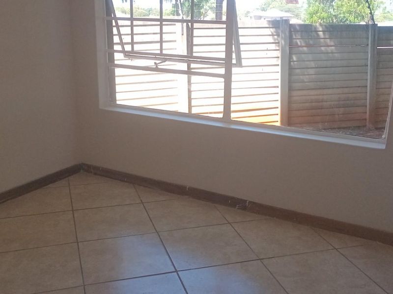 An empty bedroom featuring neutral tiled flooring, a large top-hung window, and simple skirting boards, providing a clean canvas for interior design.