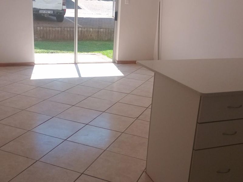 An open-plan living and kitchen area featuring tiled flooring, built-in cabinetry, and a sliding glass door providing access to the exterior.