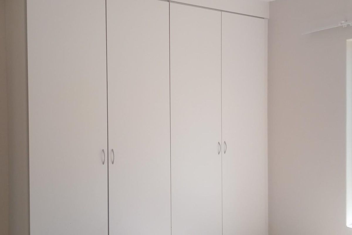A clean, empty bedroom featuring neutral walls and ample built-in cupboard storage space.