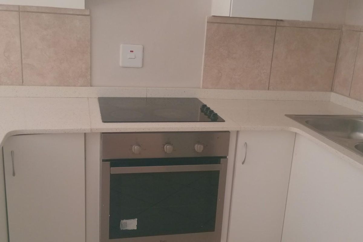 A clean, functional kitchen featuring built-in oven, electric hob, stone countertops, and a double basin sink with tiled backsplash.