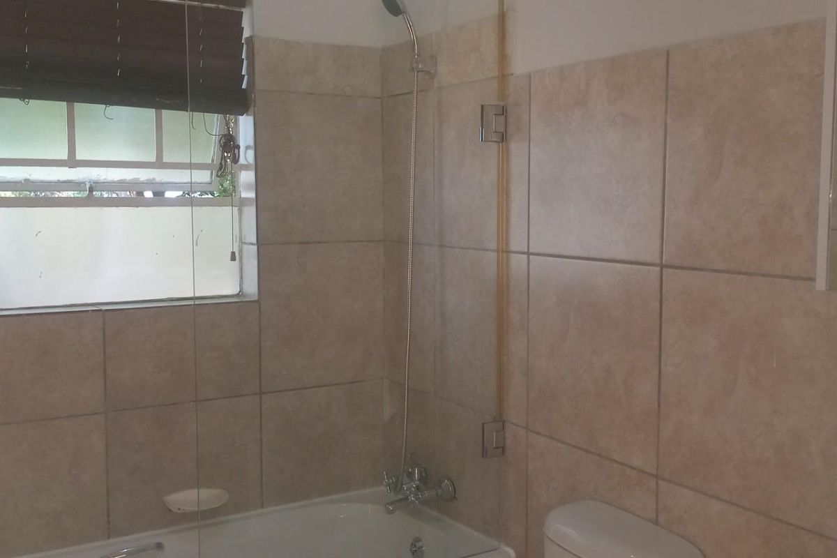 A functional bathroom featuring a bathtub with a shower mixer, glass screen, and neutral wall tiling.