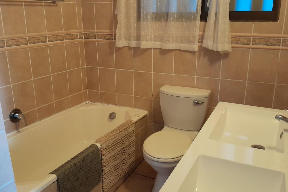 A functional bathroom featuring a built-in bathtub, a standard toilet, and a double vanity sink with tiled walls.