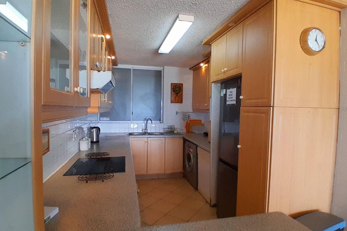 A functional kitchen featuring light wood cabinetry, tiled backsplash, integrated sink, and built-in hob, offering a practical layout for daily meal preparation.