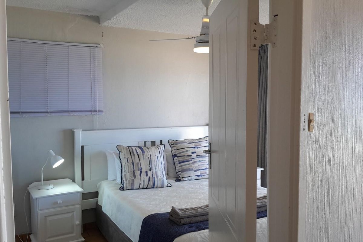 A bedroom featuring a ceiling fan, window blinds, and a door-mounted alarm switch, presented in a functional, lived-in condition.