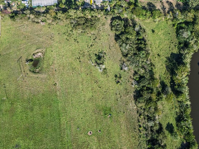Aerial view of a large, undeveloped residential land parcel featuring natural grassland, mature trees, a small pond, and direct river frontage.