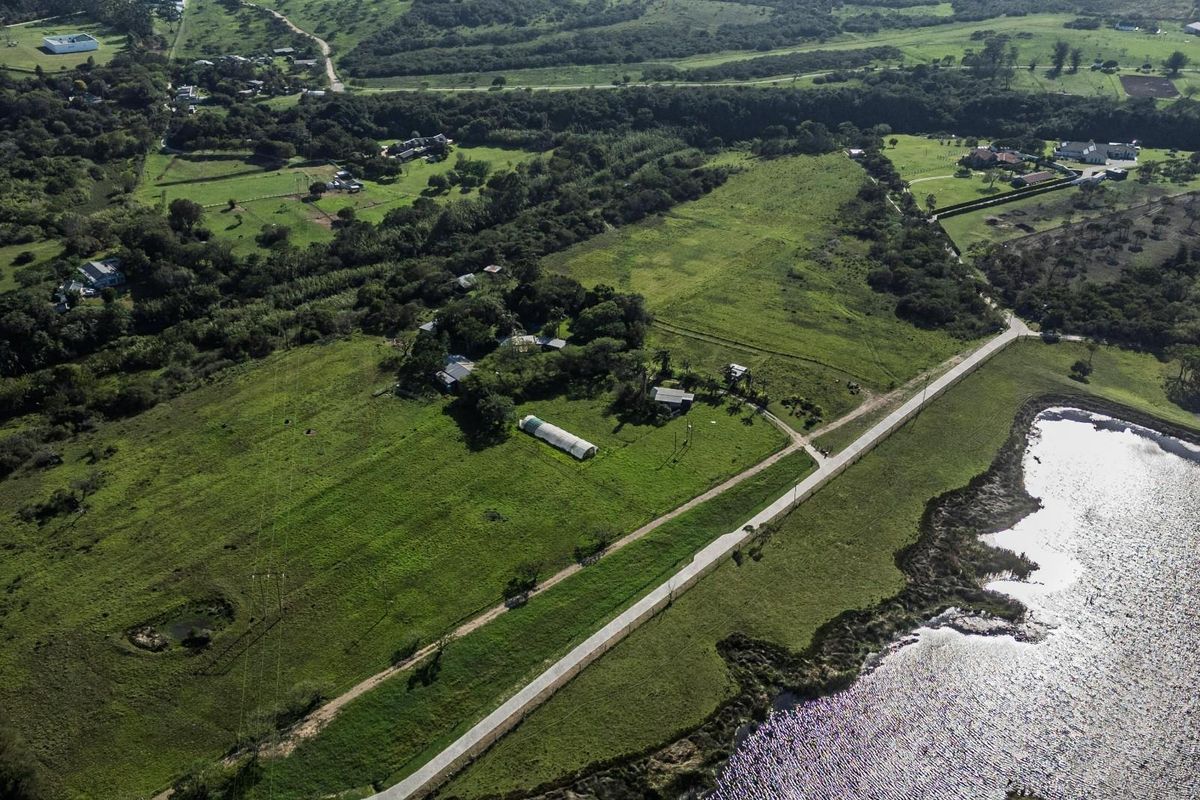 Aerial view of a large residential vacant land plot featuring open green fields, an access road, and a nearby water body.
