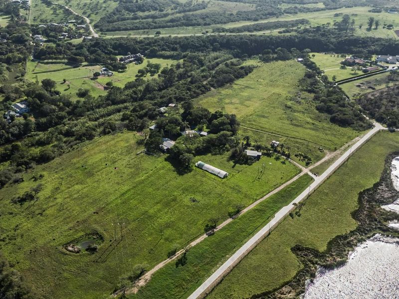 Aerial view of a large, expansive residential vacant land plot featuring rolling green fields, scattered trees, and existing small structures.
