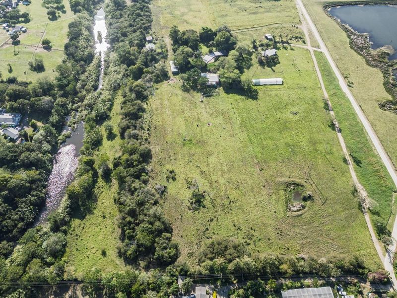 Aerial view of a large residential vacant land plot featuring natural vegetation, proximity to a river, and existing rural infrastructure.