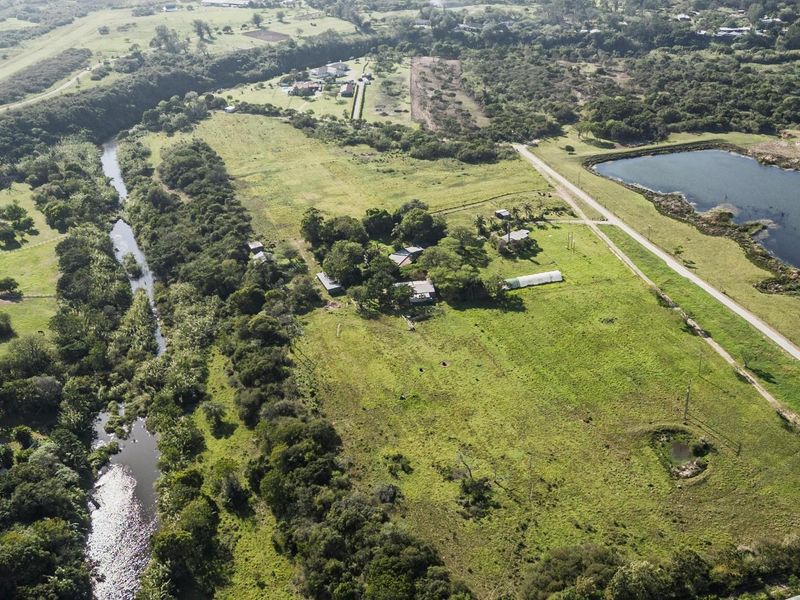 An aerial view of a large residential vacant land plot featuring natural greenery, a river, and a nearby pond.