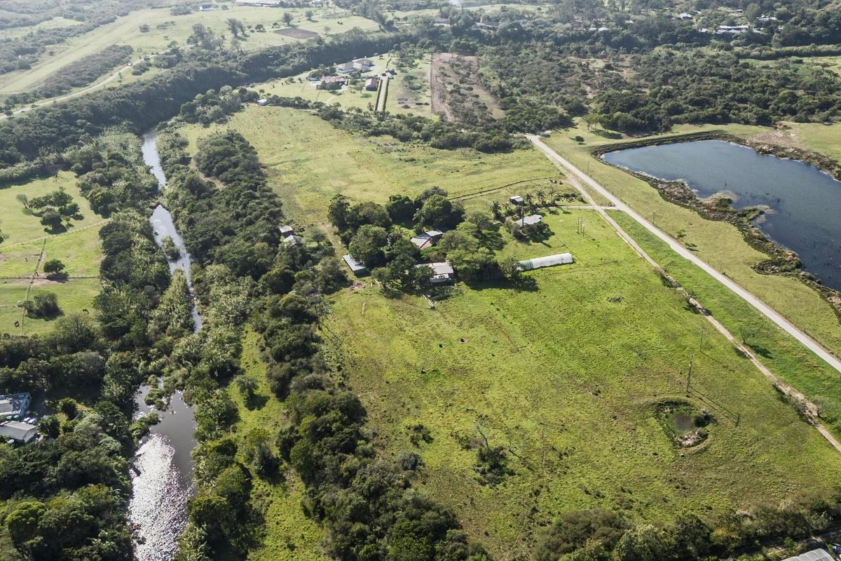 An aerial view of a large residential vacant land plot featuring natural greenery, a river, and a nearby pond.