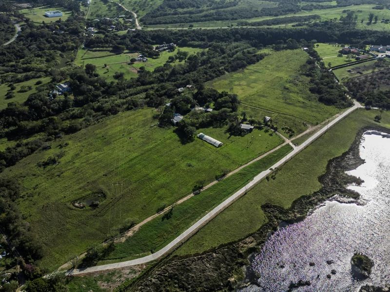 Aerial view of a large vacant residential land parcel featuring open green fields, established trees, and proximity to a water body.