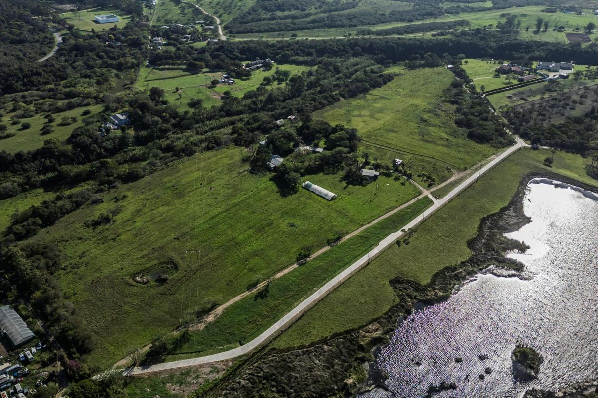 Aerial view of a large vacant residential land parcel featuring open green fields, established trees, and proximity to a water body.