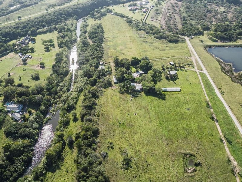 Aerial view of a large residential vacant land plot featuring natural vegetation, a river, and proximity to a nearby lake.