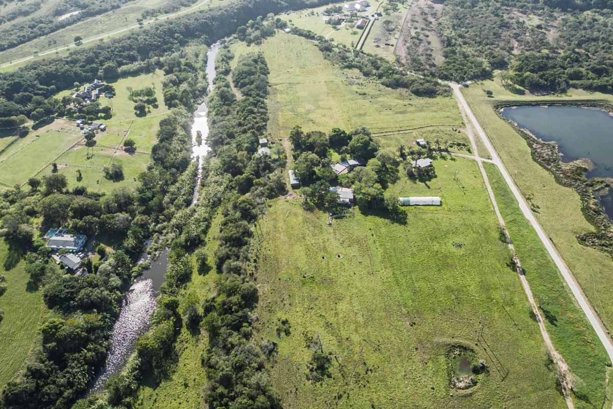 Aerial view of a large residential vacant land plot featuring natural vegetation, a river, and proximity to a nearby lake.