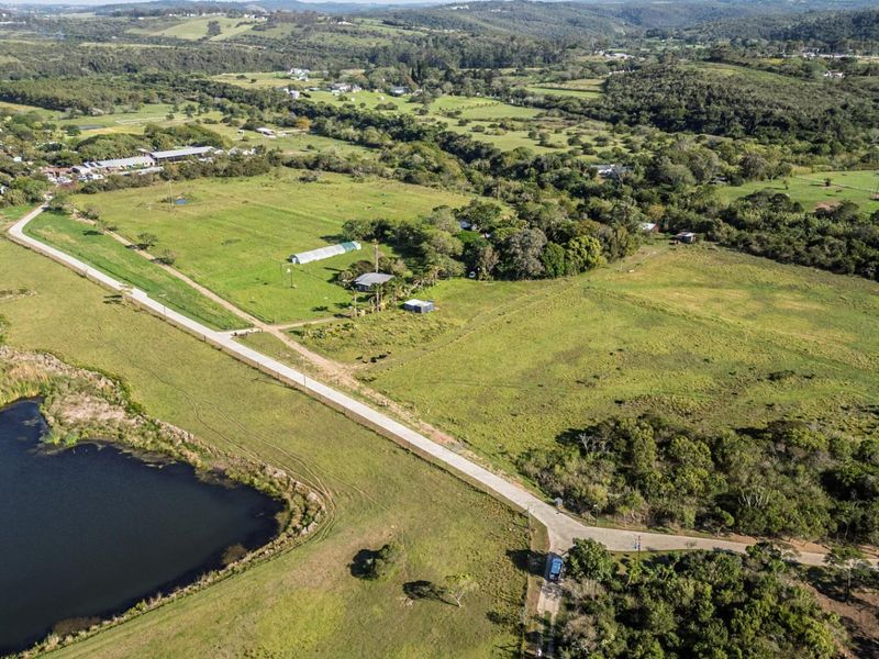 An aerial view of a large, expansive residential vacant land plot featuring lush green fields, mature trees, and proximity to a scenic water body.