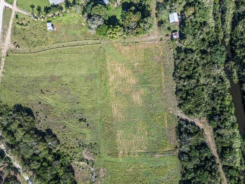 Aerial view of a vacant residential plot featuring open grassy land, bordering natural vegetation and a small water feature.