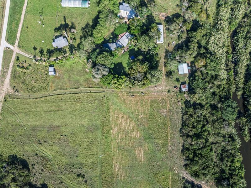 Aerial view of a large residential land parcel featuring established trees, open pasture, and existing outbuildings adjacent to a natural watercourse.