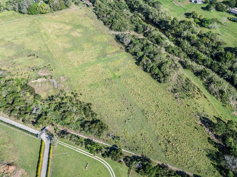 An aerial view of a large, vacant residential plot featuring expansive grassland, natural river frontage, and established access road infrastructure.